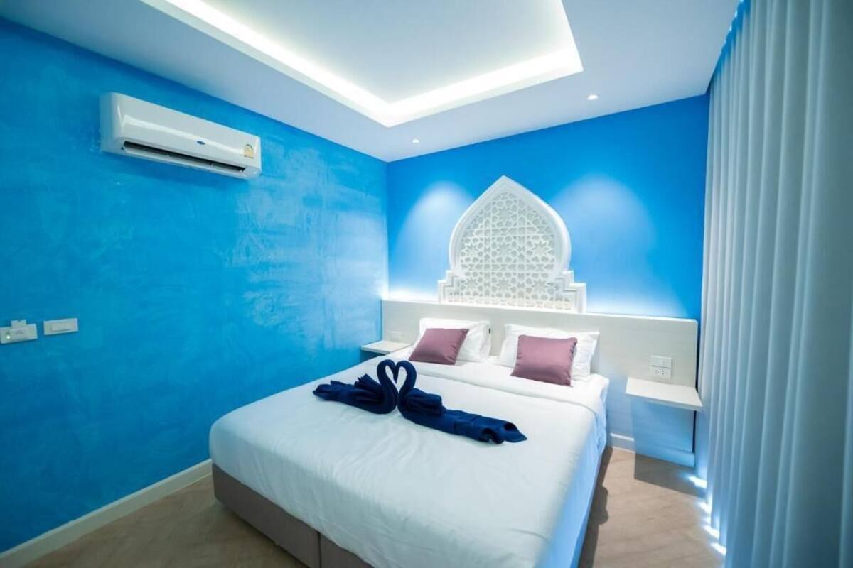 A hotel room with a large bed, a skylight, a decorative wall piece, and a modern air conditioning unit.