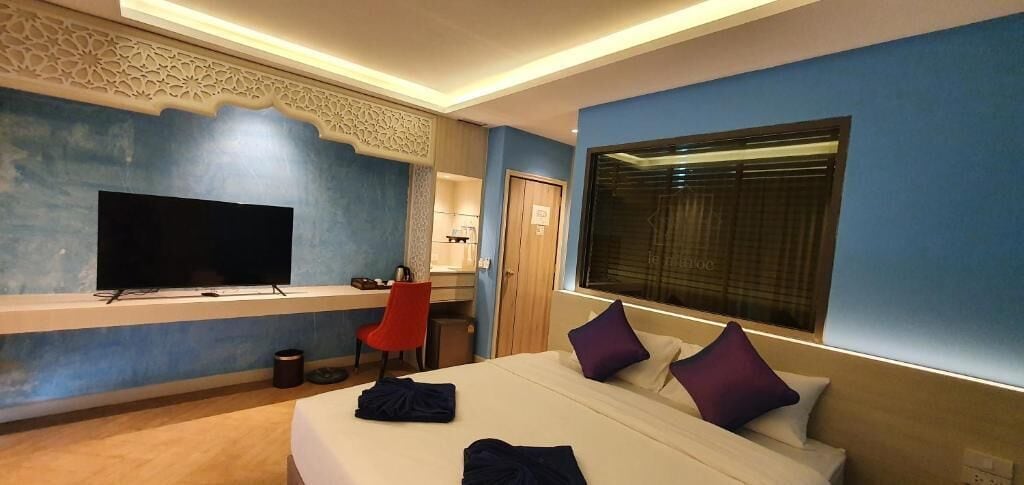 Une chambre d’hôtel dotée d’un grand lit, d’un téléviseur à écran plat fixé au mur, d’un bureau avec une chaise et d’une fenêtre avec des stores.