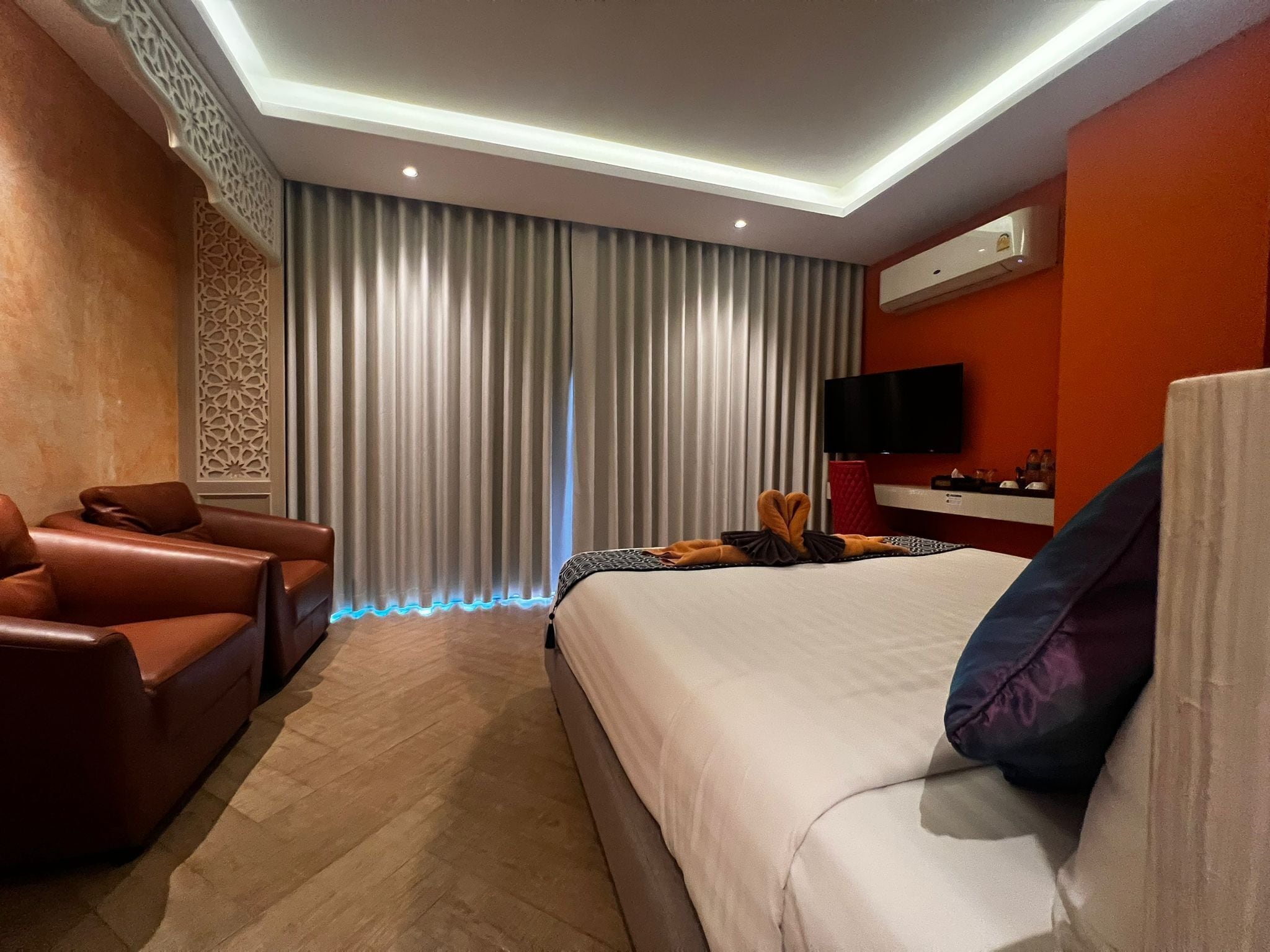 Een moderne hotelkamer met een groot bed, een leren bank, een flatscreen televisie en een decoratief wandpaneel.