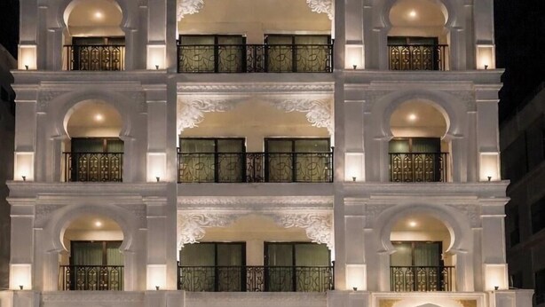 Un hotel a più piani con balconi, un ingresso centrale e posti a sedere all'aperto.