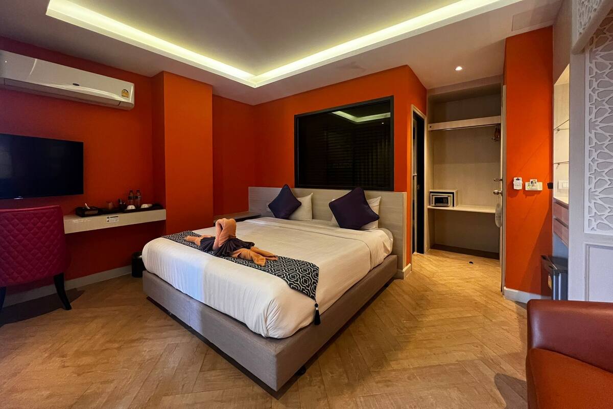 A modern hotel room with a large bed, a TV, a desk, and a wardrobe.