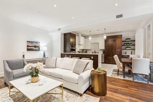 A modern living room with a white sofa, a coffee table, and a dining area with a table and chairs.