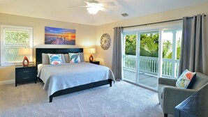 A bedroom with a bed, nightstands, a ceiling fan, a painting, and a view through a sliding glass door. - Coastal Comfort & 3/4 Time Compound (Key West)