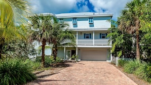 A two-story house with a garage, surrounded by lush greenery and palm trees. - Coastal Comfort & 3/4 Time Compound (Key West)