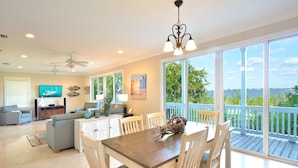 A spacious living area with a dining table, white chairs, and a view of the ocean through large windows. - Coastal Comfort & 3/4 Time Compound (Key West)