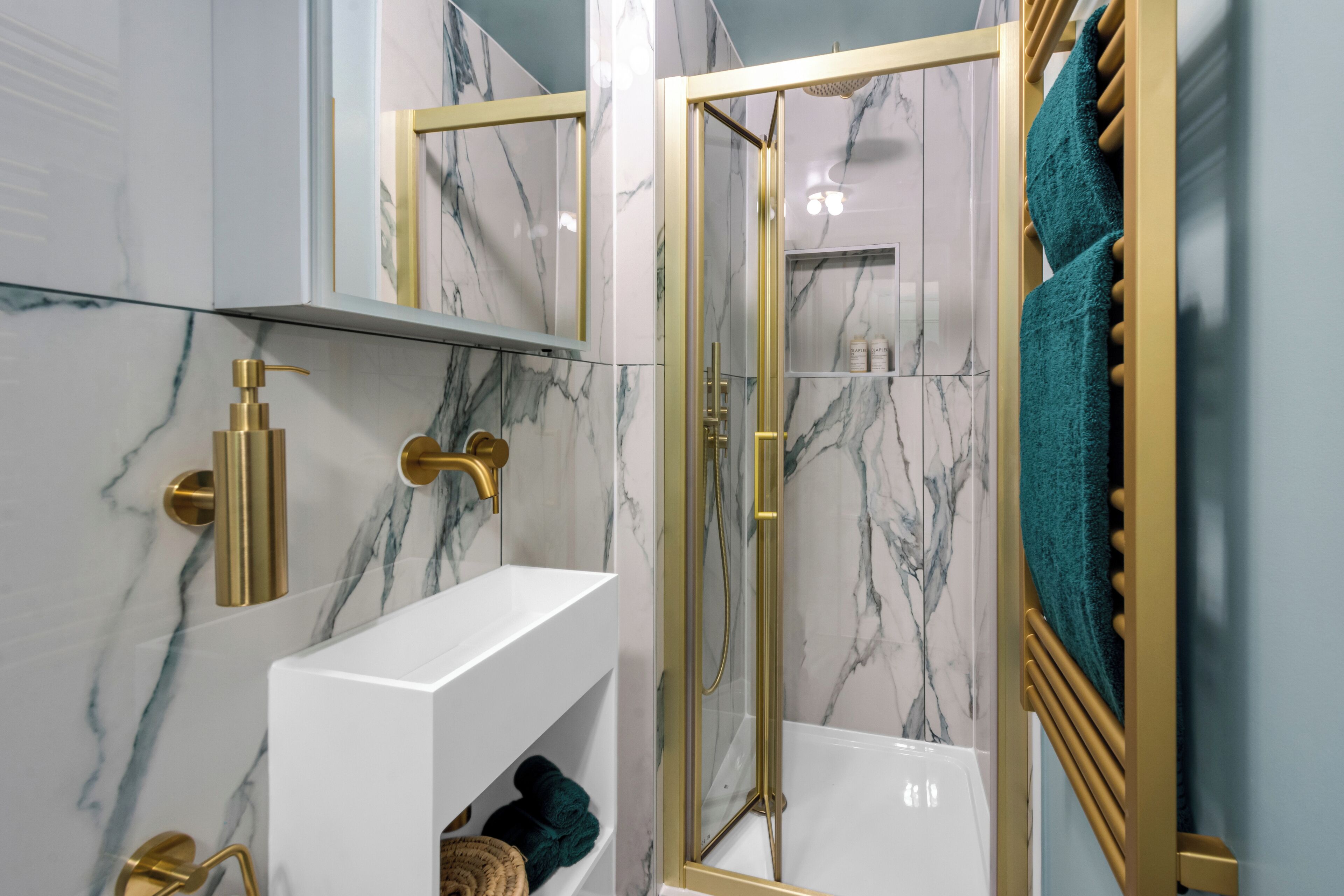 Une salle de bain moderne avec des murs en marbre, un meuble-lavabo blanc, des accessoires dorés et une douche à parois de verre.