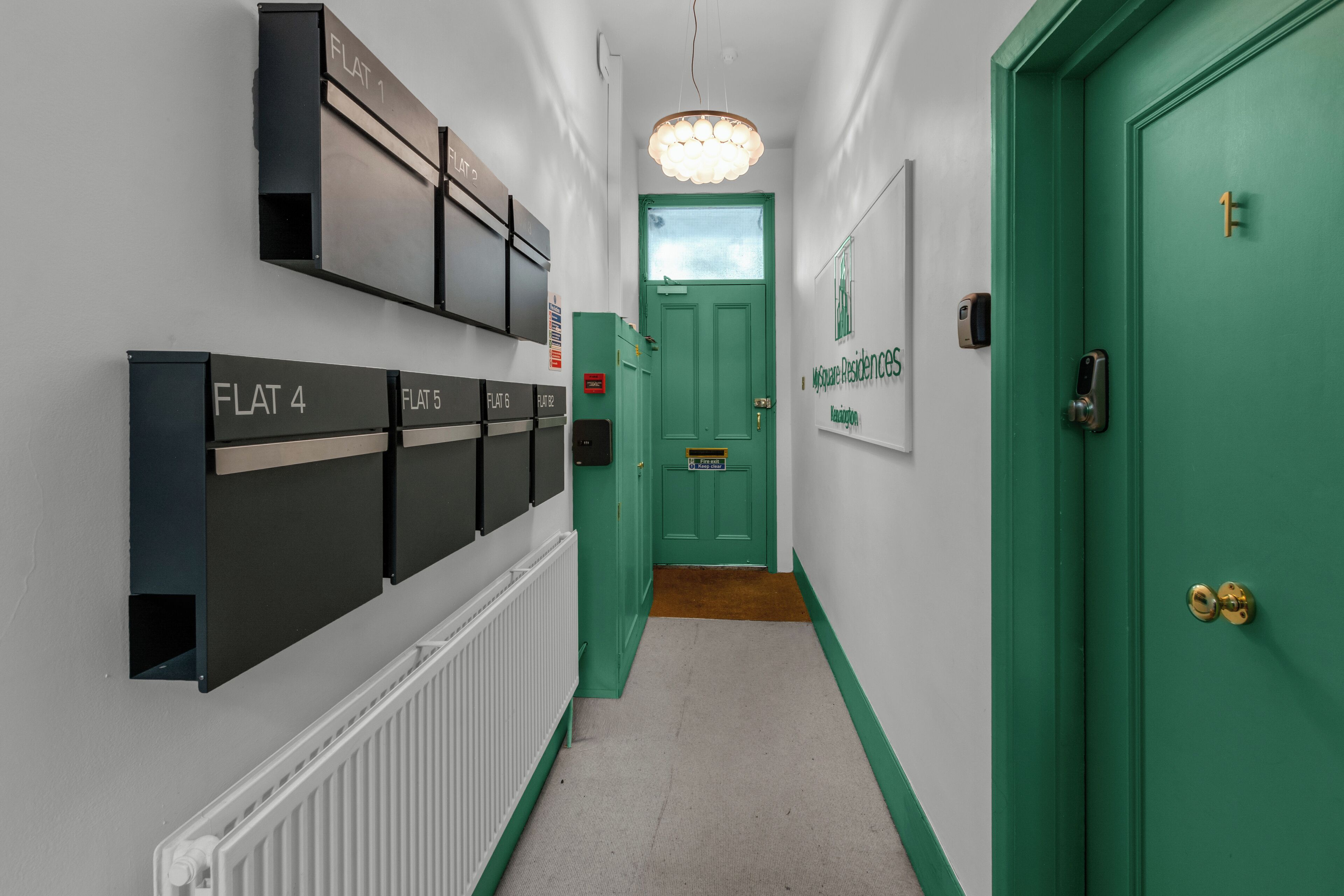 En gang med en grøn dør, et skilt med 'Lejlighed 1' og et skilt med 'McQueen Residences'.