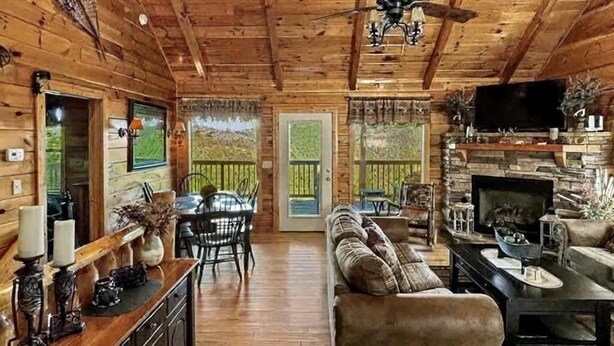 A wooden cabin interior with a dining area, sofa, fireplace, and ceiling fan.