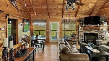 Interior de una cabaña de madera con comedor, sofá, chimenea y ventilador de techo.