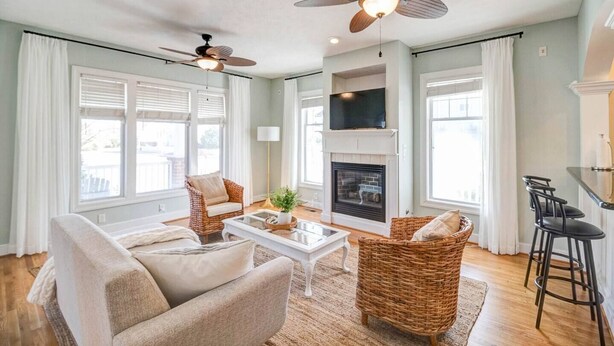 A spacious living room with a fireplace, two ceiling fans, wicker furniture, and a dining area with bar stools. - Convenient | 2 King Beds l Fast Wifi (Norfolk)