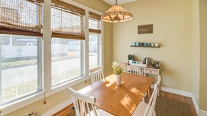 A dining area with a wooden table and white chairs, large windows with bamboo blinds, a hanging light fixture, and a coffee station with a kettle and cups. - Convenient | 2 King Beds l Fast Wifi (Norfolk)