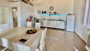 A modern kitchen with white cabinets, a dining table with a white tablecloth, and a variety of kitchen appliances. - Villa Fiori with pool by Wonderful Italy (Olbia)