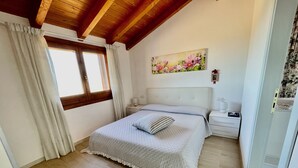 A bedroom with a bed, a nightstand, a window with curtains, a painting on the wall, and a wooden ceiling. - Villa Fiori with pool by Wonderful Italy (Olbia)