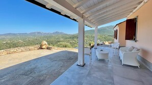 A covered outdoor seating area with white wicker furniture and a view of green hills and mountains. - Villa Fiori with pool by Wonderful Italy (Olbia)