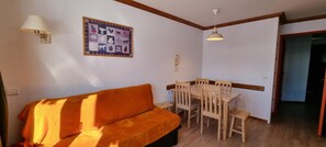 A living room with a sofa, a dining table with chairs, a wall-mounted lamp, and a framed picture.