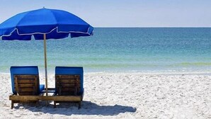 Una spiaggia con due lettini di legno sotto un ombrellone blu.