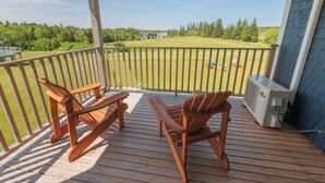 Una terraza de madera con dos sillas Adirondack y un equipo de aire acondicionado.