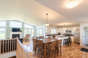 Une cuisine spacieuse avec un plancher en bois, un coin repas doté d’une grande table et de chaises, et une cheminée.