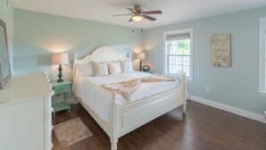A bedroom with a bed, nightstands, a ceiling fan, a window, and a wall decoration. - Storybook Island Cottage at The Gables of PEI (Stanley Bridge)
