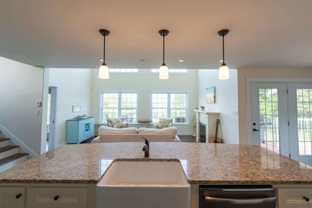 A kitchen with granite countertops, a white sink, pendant lights, and a view of the outside.