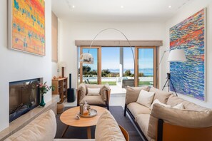 A modern living room with a fireplace, a coffee table, a sofa, and a large window offering a view of the outdoors.