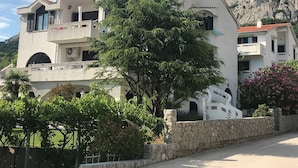 Un bâtiment moderne à la façade blanche, doté de nombreux balcons et d’un mur en pierre à l’avant.