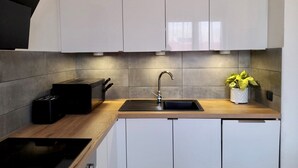 Une cuisine moderne avec des armoires blanches, une cuisinière noire et un évier avec un robinet. On peut voir une plante en pot sur le plan de travail.