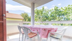Une terrasse extérieure couverte, avec une table ronde et quatre chaises, chacune ornée d’un coussin à motif différent.