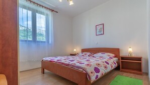 A bedroom with a wooden bed, two bedside tables with lamps, a green rug, and a window with sheer curtains.