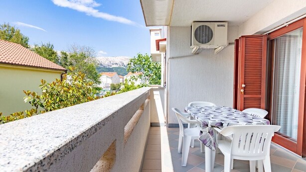 A balcony with a table and chairs, a red door, and an air conditioning unit.
