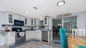 A modern kitchen with white cabinets, a microwave, oven, and dishwasher. There is a sign that reads "BEACH HOUSE" and a dining area with a wooden table and chairs. - Tropical house and pool - 1/2 mile away from beach (South Venice)