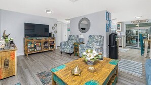 A living room with a television, patterned armchairs, a coffee table with decorative items, and a bookshelf. - Tropical house and pool - 1/2 mile away from beach (South Venice)