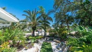 A well-maintained garden with palm trees, a gravel path, and a wooden bench. - Tropical house and pool - 1/2 mile away from beach (South Venice)