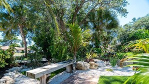 A garden with a wooden bench, gravel path, and various plants. - Tropical house and pool - 1/2 mile away from beach (South Venice)