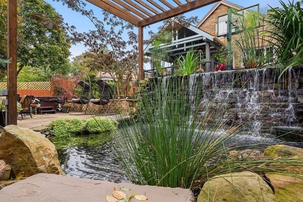 Ein Garten mit einem kleinen Wasserfall, einer Pergola und einer Holzterrasse.