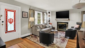 A living room with a sofa, two armchairs, a coffee table, a fireplace, and a TV mounted on the wall. - Hoosier Haven Spacious Retreat (Bloomington)