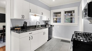 A modern kitchen with white cabinets, a black countertop, and a built-in stove. - Hoosier Haven Spacious Retreat (Bloomington)