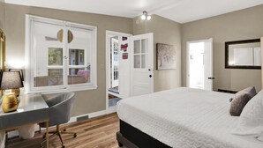 A bedroom with a bed, a desk, and a chair. There are two doors and a window with blinds. - Hoosier Haven Spacious Retreat (Bloomington)