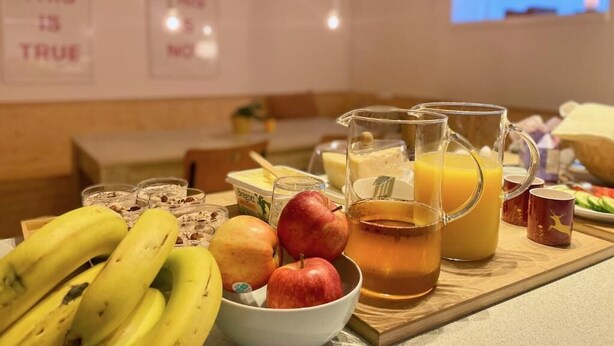 A breakfast setting with fruits, a pitcher of tea, and a glass of orange juice on a wooden table. - HEMMET - Simrishamns vandrarhem och B&B (Simrishamn)