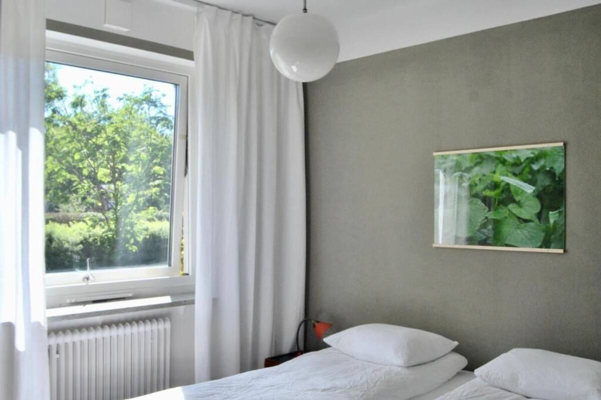 A bedroom with a bed, a window with curtains, a radiator, and a wall-mounted picture.