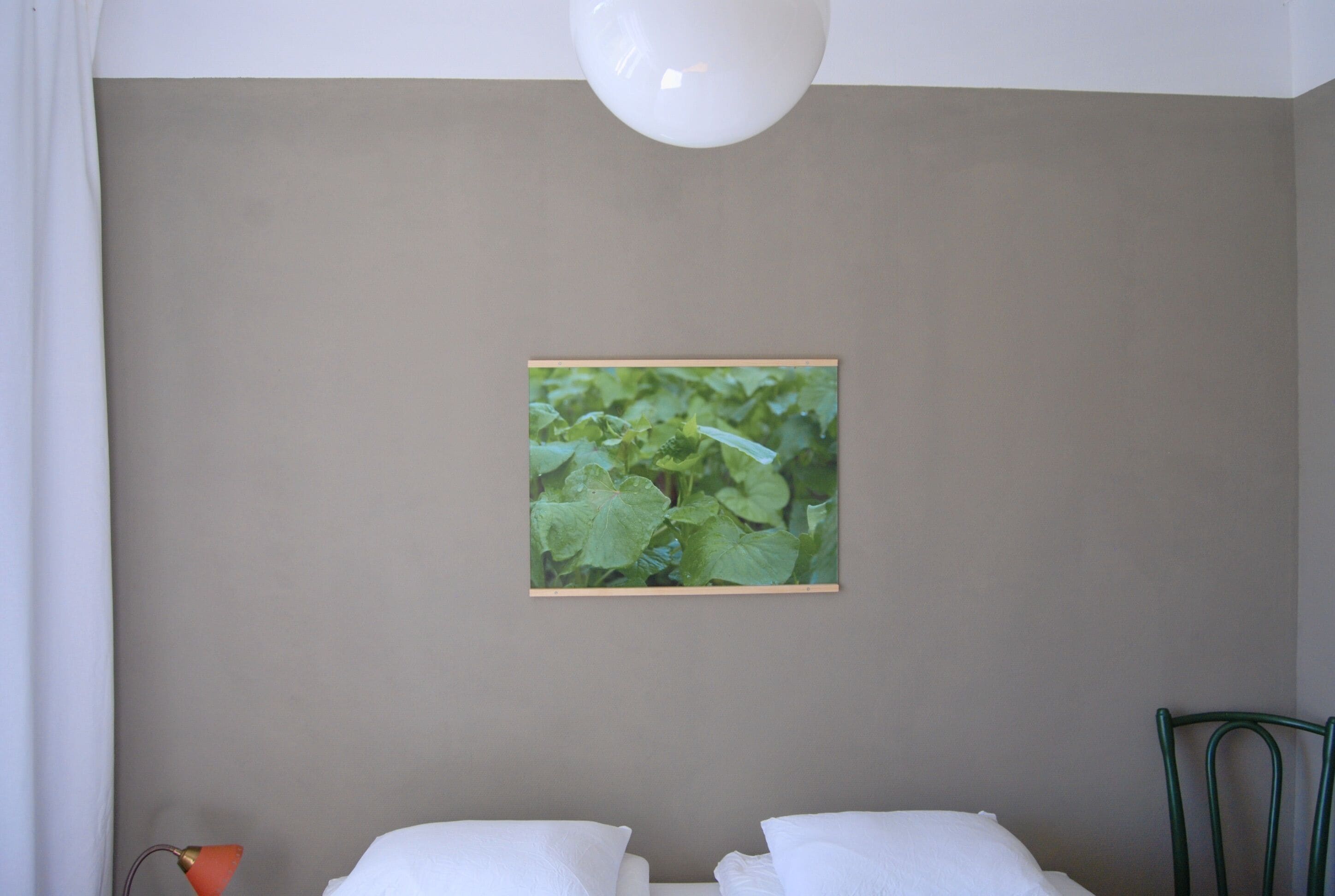 Een slaapkamer met een bed, nachtkastje, lamp en een lijst aan de muur.