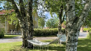 A hammock between two trees in a grassy area with a building in the background. - HEMMET - Simrishamns vandrarhem och B&B (Simrishamn)