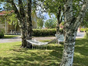 Un'amaca tesa tra due alberi in una zona erbosa, con un edificio sullo sfondo.