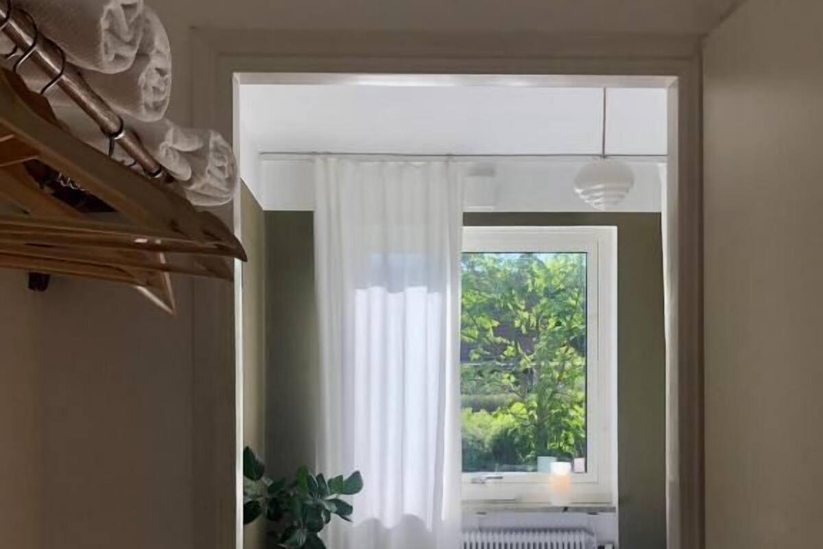 A bedroom with a bed, a window with curtains, a radiator, and a potted plant.