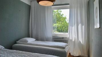 Un dormitorio con dos camas, una ventana con cortinas, un radiador y una lámpara colgante.