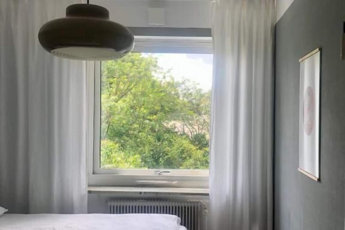 A bedroom with two beds, a radiator, a window with curtains, and a hanging light fixture.