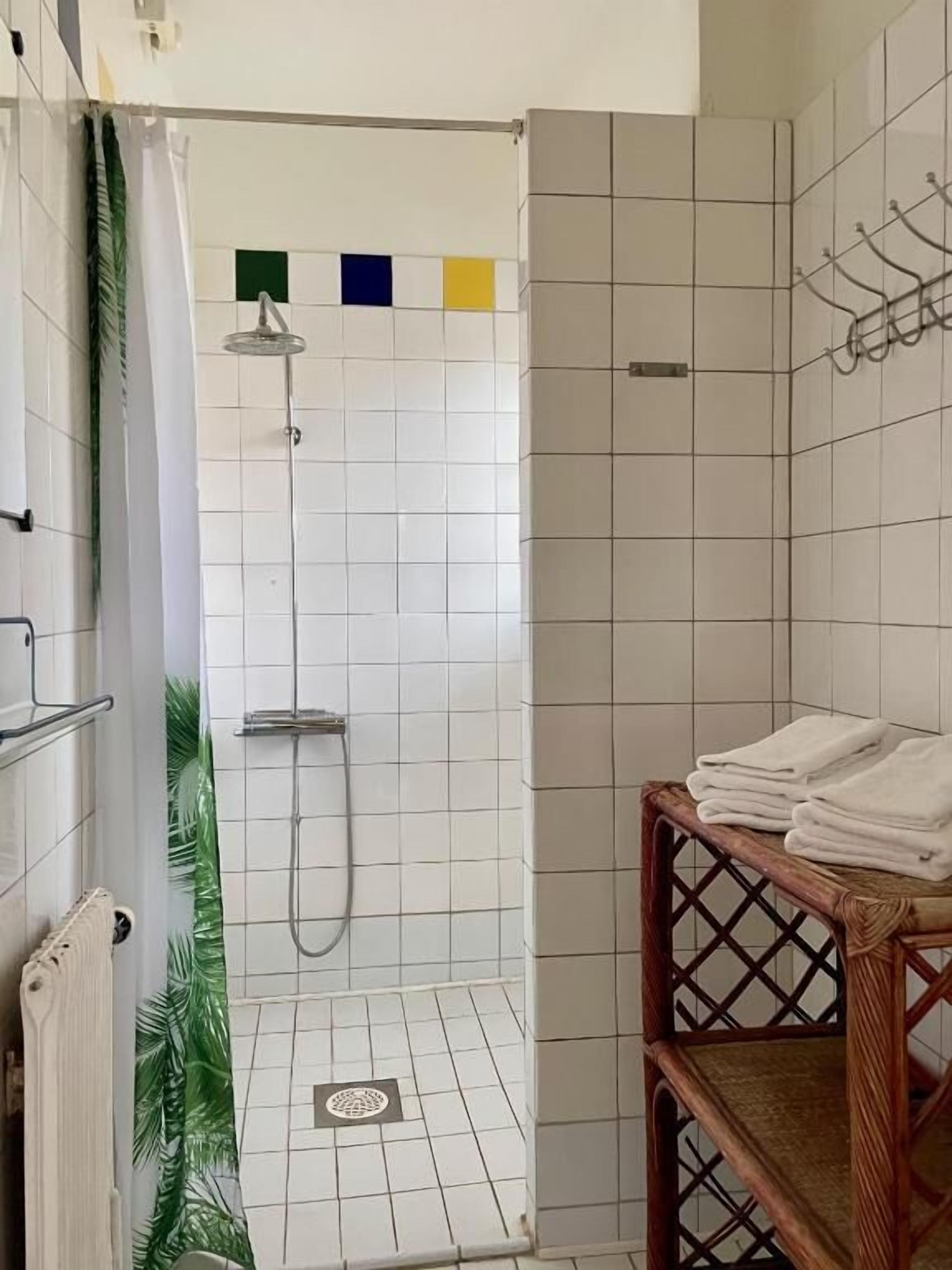 Uma área de chuveiro com parede revestida de azulejos, um chuveiro e um porta-toalhas.