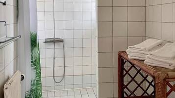 Uma área de chuveiro com parede revestida de azulejos, um chuveiro e um porta-toalhas.