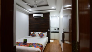 Une chambre d’hôtel avec un lit, un ventilateur de plafond, un appareil de climatisation, une petite kitchenette et un plancher en bois.