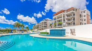 A swimming pool with lounge chairs, a building with balconies, and palm trees. - Blue Maho Sxm (Sint Maarten)